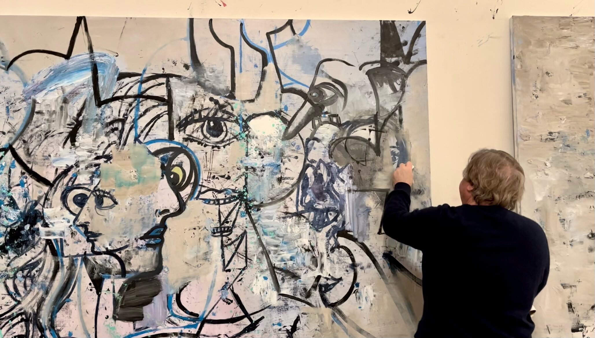 back of a man painting in his studio, with an image of various faces