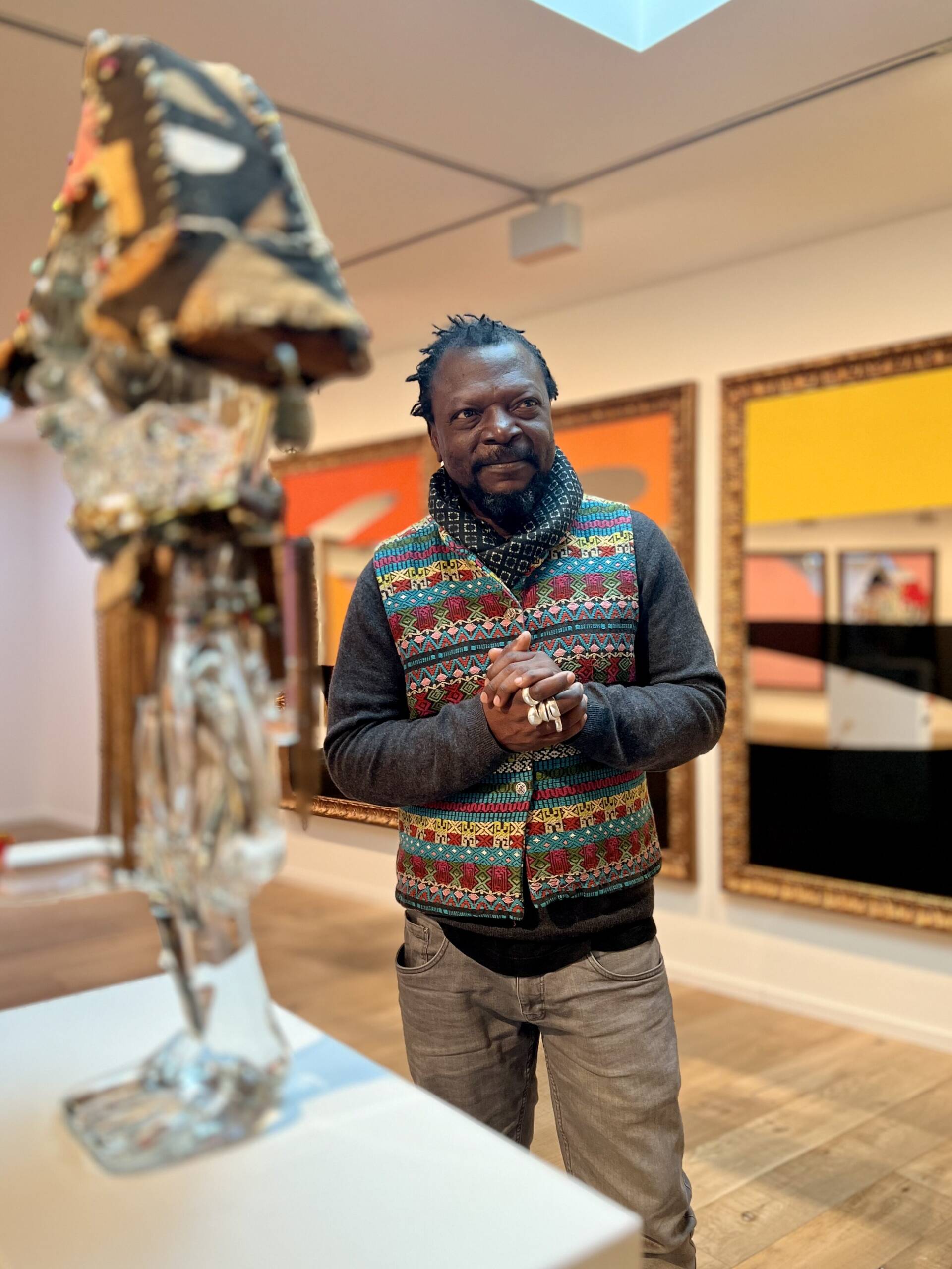 a man stands behind a sculpture in a bright yellow gallery.